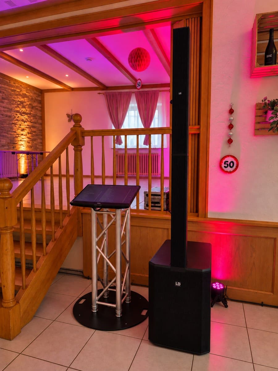 Musiktheke mit Lautsprechersäule und Touchscreen im Saal einer Geburtstagsfeier, in pinkes Licht getaucht