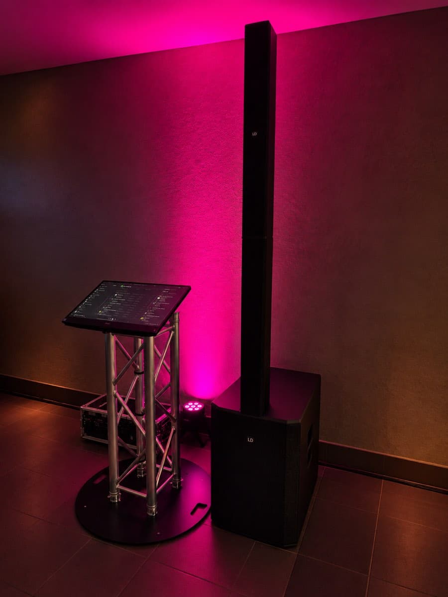 Musiktheke mit Touchscreen auf Traversenständer und hoher Lautsprechersäule vor einer pinken Wand