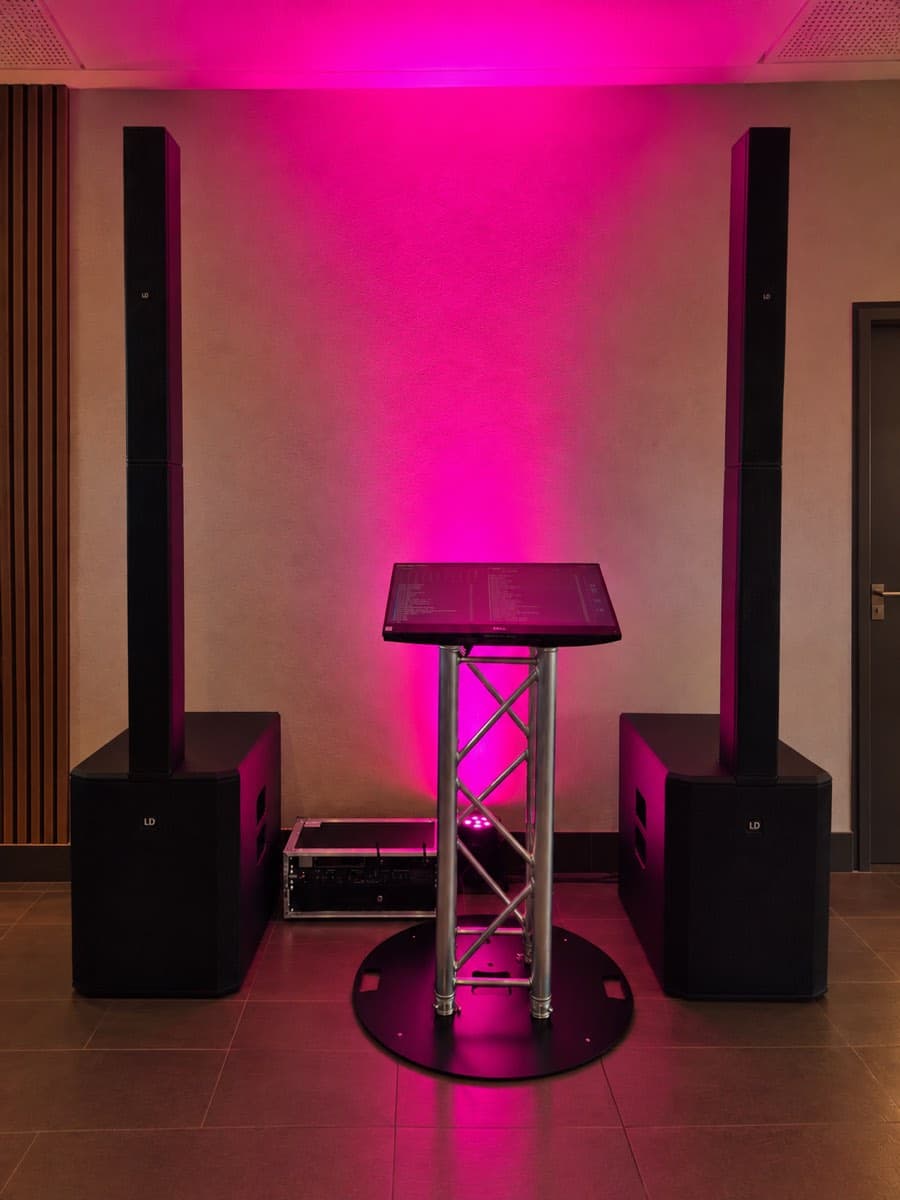 Musiktheke zwischen zwei Lautsprechersäulen vor einer pink beleuchteten Wand