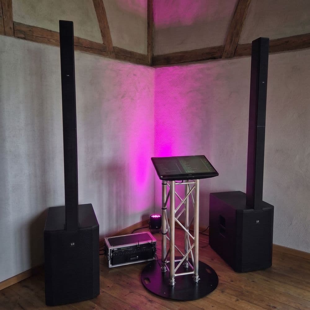 Musiktheke mit zwei Lautsprechersäulen in einem Raum mit Holzbalken und pinkem Licht